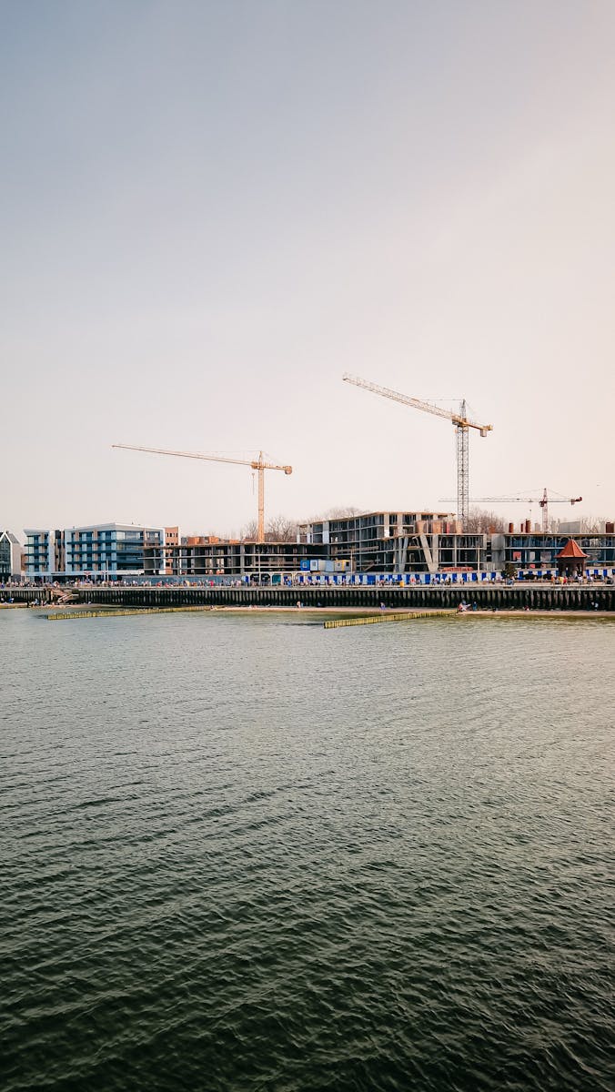 A scenic riverfront construction site with cranes against a clear sky, showcasing urban development.