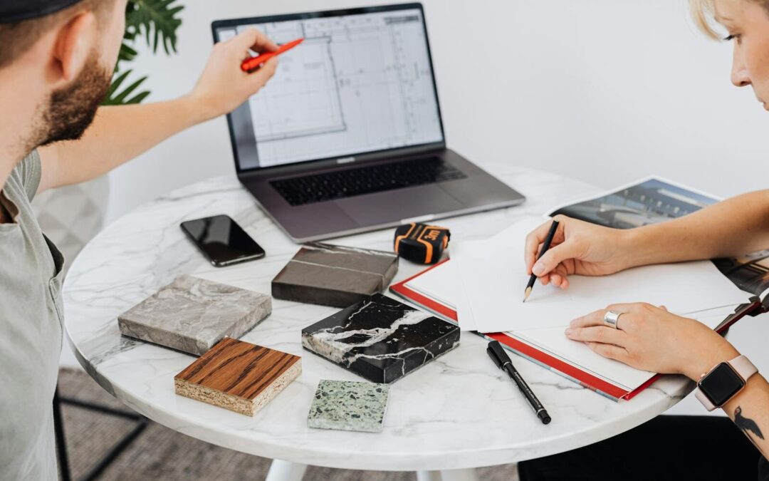Two designers collaborate on a project with laptop and material samples on a marble table.